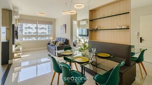 A modern living room with a glass dining table, green chairs, and a sofa.