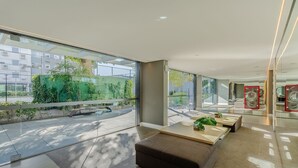 A modern hotel lobby with large windows, a seating area with a bench and tables, and a view of the street outside.