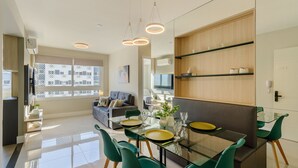 A modern living room with a glass dining table, green chairs, and a sofa. - Apto c\/ Churrasqueira e Garagem POA GPL1305 (Porto Alegre)