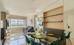 A modern living room with a glass dining table, green chairs, and a sofa. - Apto c\/ Churrasqueira e Garagem POA GPL1305 (Porto Alegre)