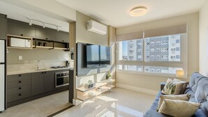 A modern kitchen with built-in appliances, a flat-screen TV, and a dining area with a sofa and cushions. - Apto c\/ Churrasqueira e Garagem POA GPL1305 (Porto Alegre)