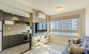 A modern kitchen with built-in appliances, a flat-screen TV, and a dining area with a sofa and cushions. - Apto c\/ Churrasqueira e Garagem POA GPL1305 (Porto Alegre)