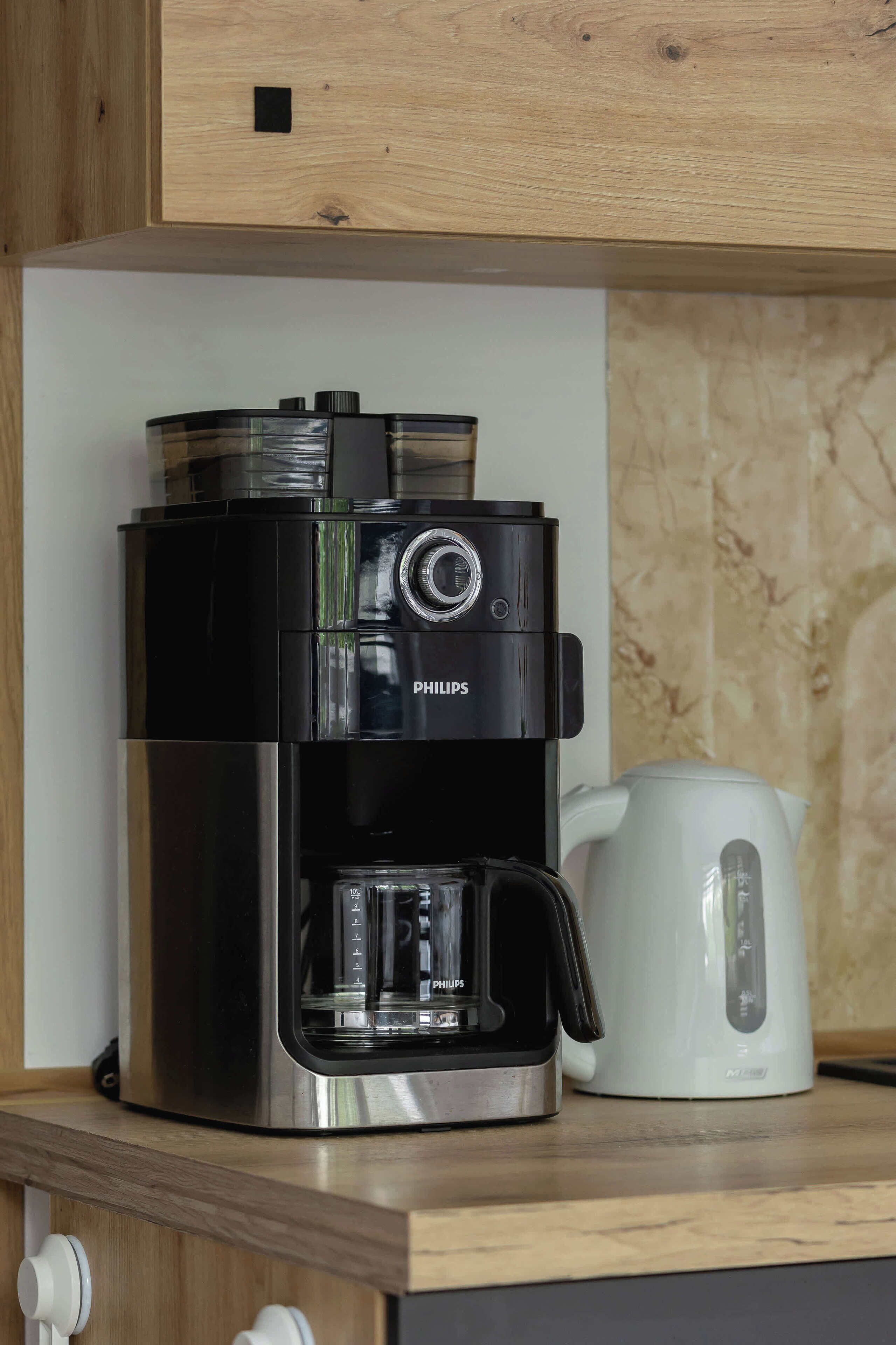 Une machine à café noire de marque Philips est posée sur un comptoir en bois, à côté d’une bouilloire électrique blanche.