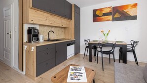 A modern kitchen with wooden cabinets, a coffee maker, and a dining area with a table and chairs. - Comfortable Apartment | Balcony | Close to Silesian Park (Katowice)