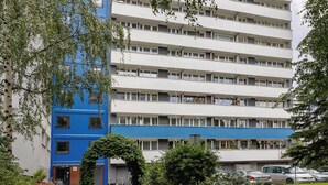A multi-story building with a blue and white facade, surrounded by greenery and a paved pathway leading to the entrance. - Comfortable Apartment | Balcony | Close to Silesian Park (Katowice)