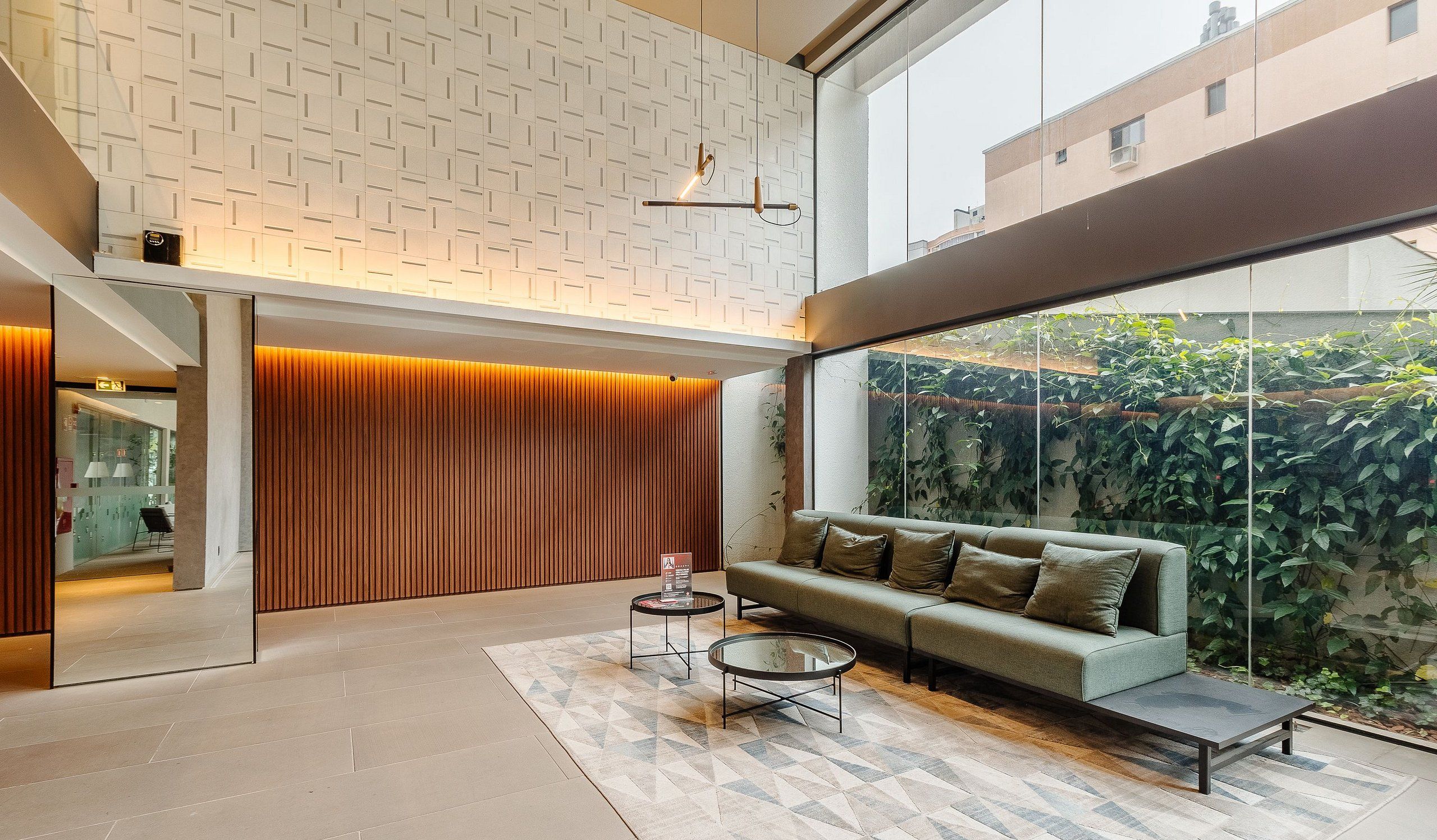 A modern interior with a sofa, two coffee tables, a patterned wall, and a large window overlooking greenery.