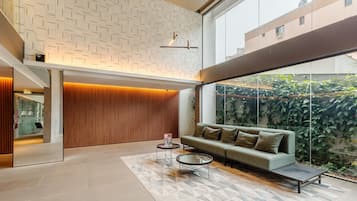 A modern interior with a sofa, two coffee tables, a patterned wall, and a large window overlooking greenery.
