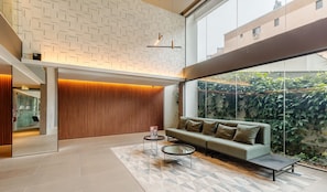 A modern interior with a sofa, two coffee tables, a patterned wall, and a large window overlooking greenery. - Charming Studio With Pool in POA Grb0917 (Porto Alegre)