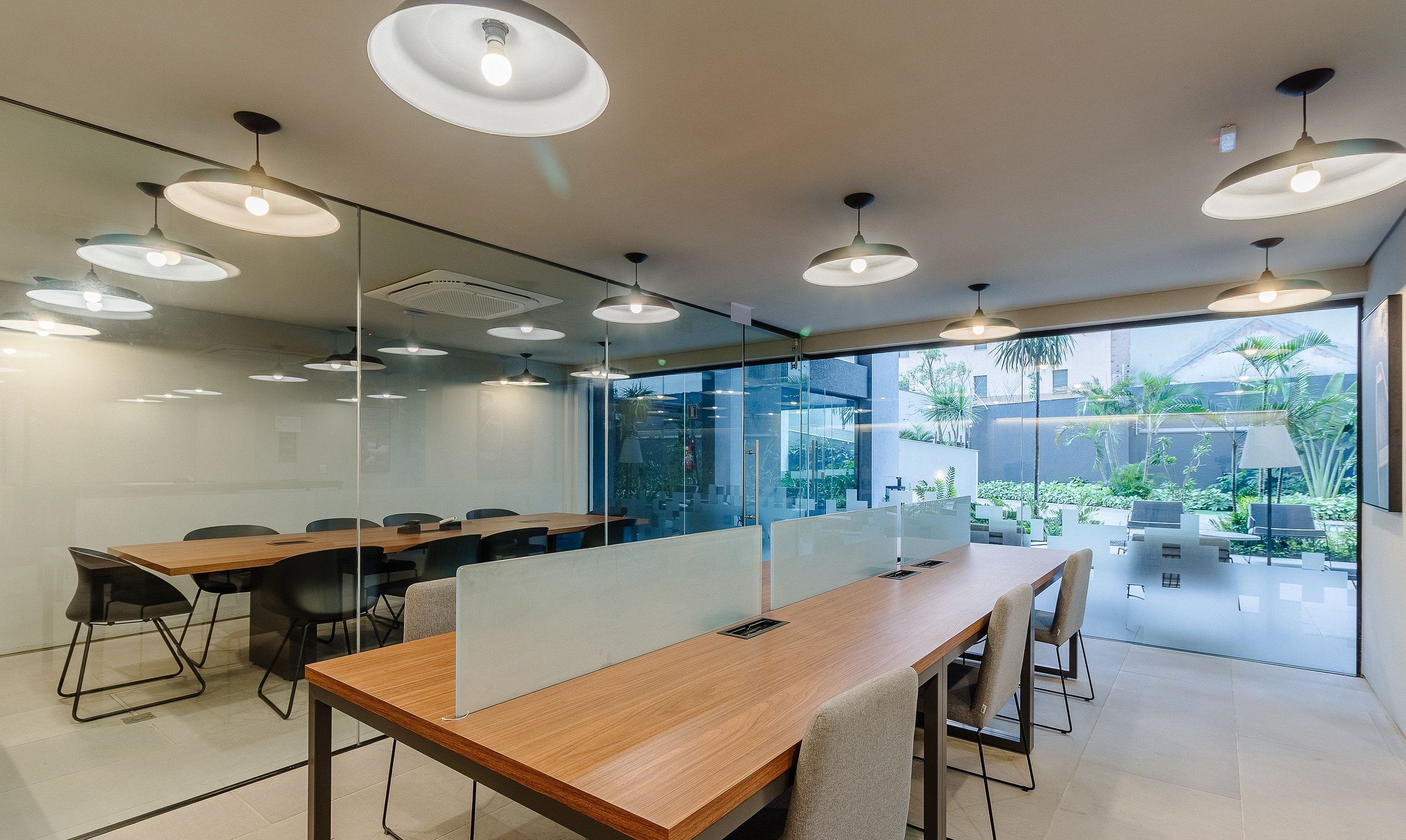 A modern conference room with glass partitions, wooden tables, and multiple pendant lights.