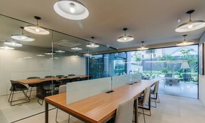 A modern conference room with glass partitions, wooden tables, and multiple pendant lights.