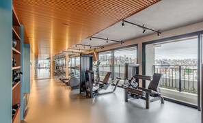 Een fitnessruimte met cardioapparaten, gewichtbanken en uitzicht op de stad door grote ramen.