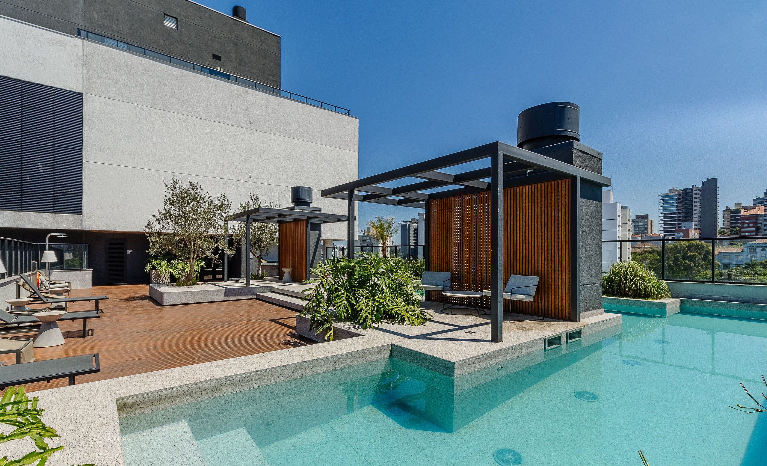 A rooftop pool area with lounge chairs, a pergola, and a view of the city skyline.