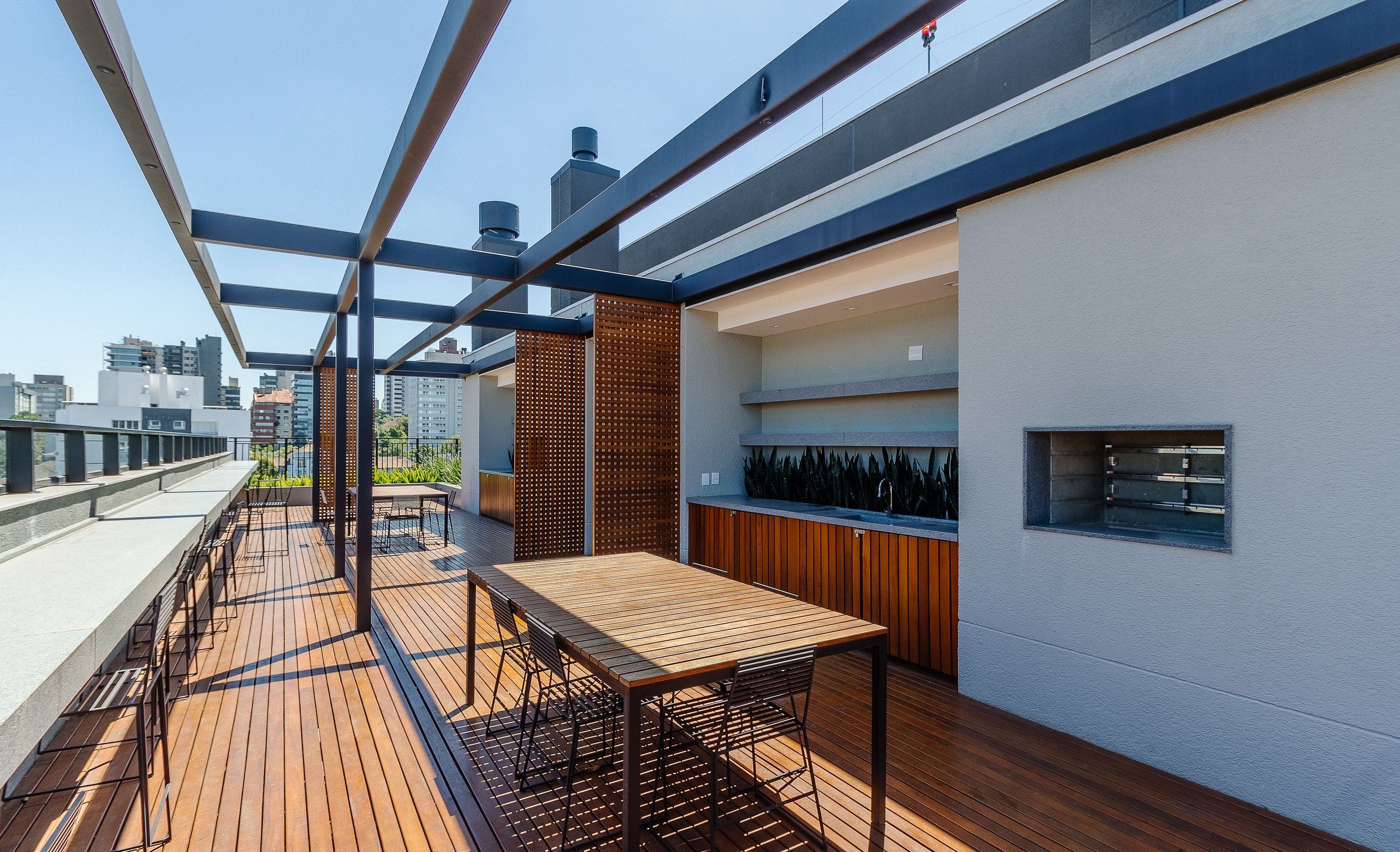 Terraza en la azotea con piso de madera, barandilla de metal y una mesa con sillas.