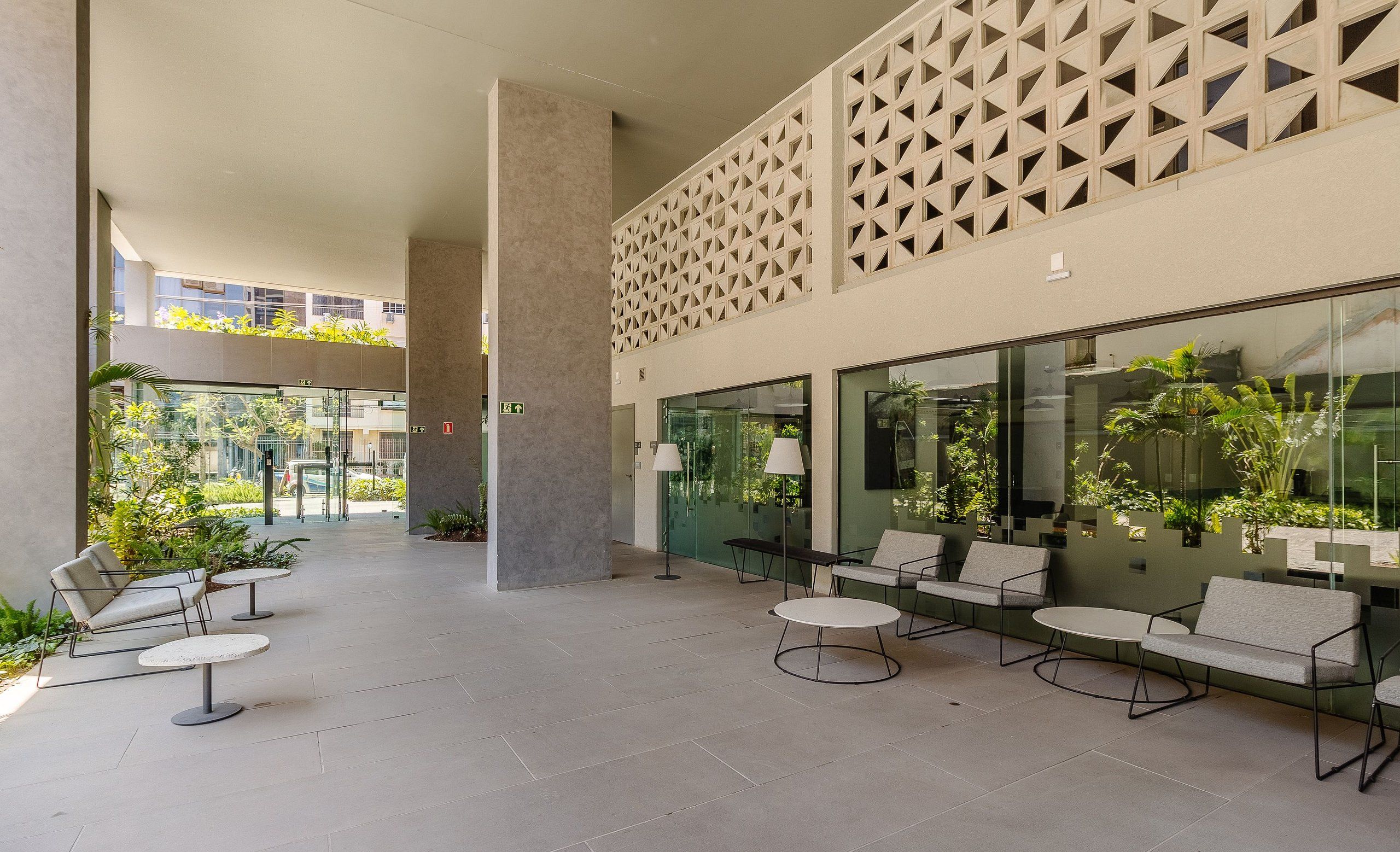 A modern outdoor seating area with tables and chairs, a geometric wall design, and large windows overlooking greenery.