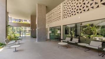 A modern outdoor seating area with tables and chairs, a geometric wall design, and large windows overlooking greenery.