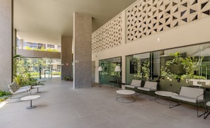 A modern outdoor seating area with tables and chairs, a geometric wall design, and large windows overlooking greenery. - Charming Studio With Pool in POA Grb0917 (Porto Alegre)