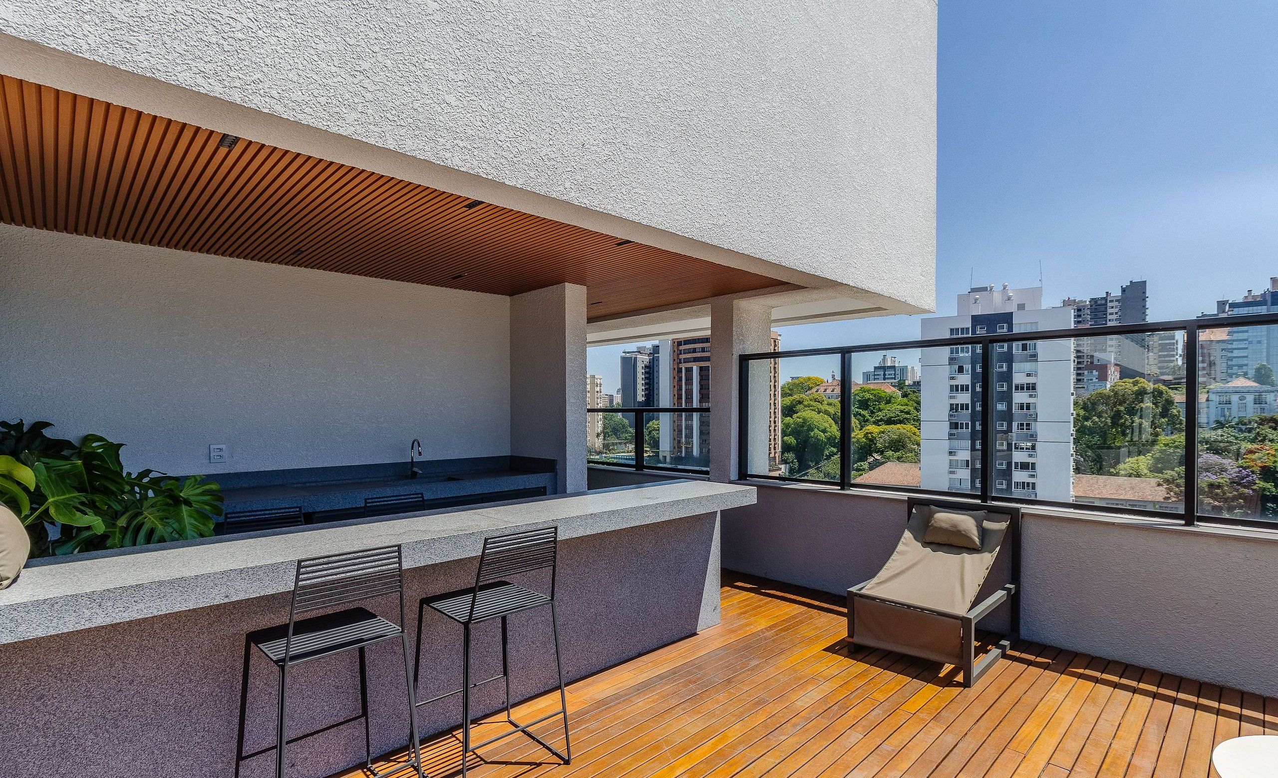 A modern outdoor balcony with a wooden floor, a bar area with two chairs, and a sofa.