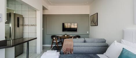 A modern hotel room with a kitchenette, a dining area, a sofa bed, and a TV.