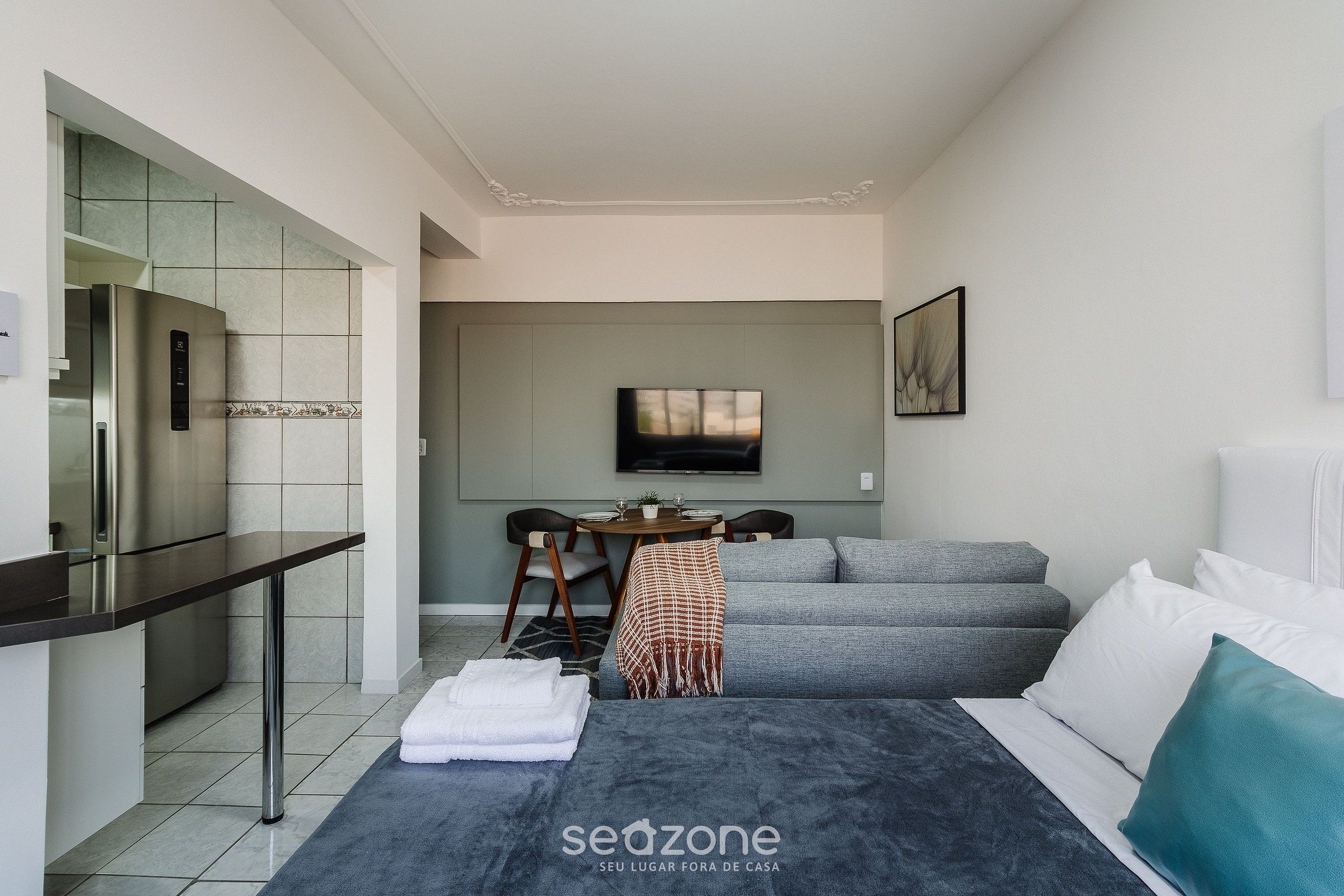 A modern hotel room with a kitchenette, a dining area, a sofa bed, and a TV.
