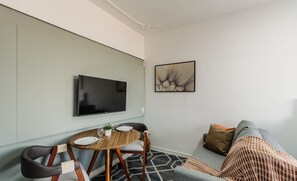 A modern living room with a flat-screen TV mounted on the wall, a round dining table with chairs, a sofa, and a patterned rug. - Practical Studio Near Farroupilha Park Hpn707 (Porto Alegre)