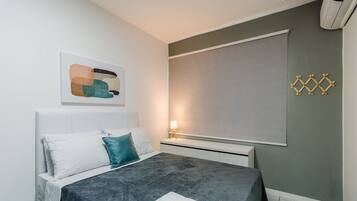 Een moderne slaapkamer met een bed, kussens, een nachtkastje met een lamp en een wandairconditioner.