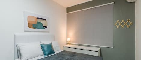 A modern bedroom with a bed, pillows, a bedside table with a lamp, and a wall-mounted air conditioner.