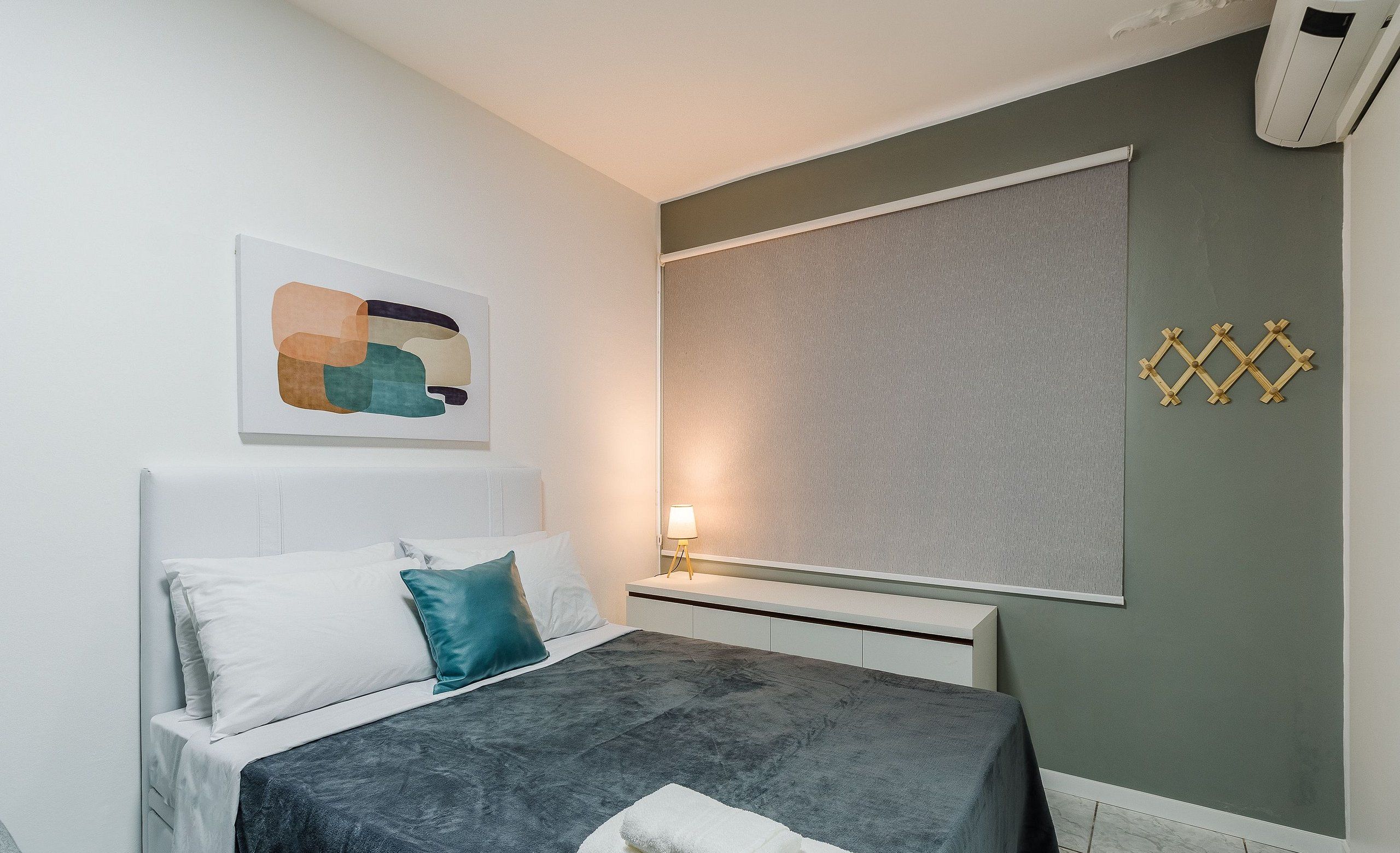 Quarto moderno com cama, almofadas, mesa de cabeceira com abajur e ar condicionado fixado na parede.
