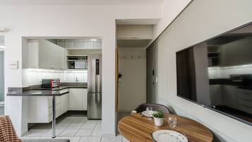 Una cucina moderna con mobili bianchi, un frigorifero in acciaio inossidabile e un forno integrato. C'è una zona pranzo con un tavolo rotondo in legno, un piatto bianco e un bicchiere d'acqua.
