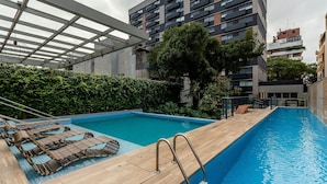 A rooftop swimming pool with wooden loungers and metal ladders, surrounded by greenery and modern buildings. -  Luxury and Sophisticated Studio Apartment with Garage LBO203 (Porto Alegre)