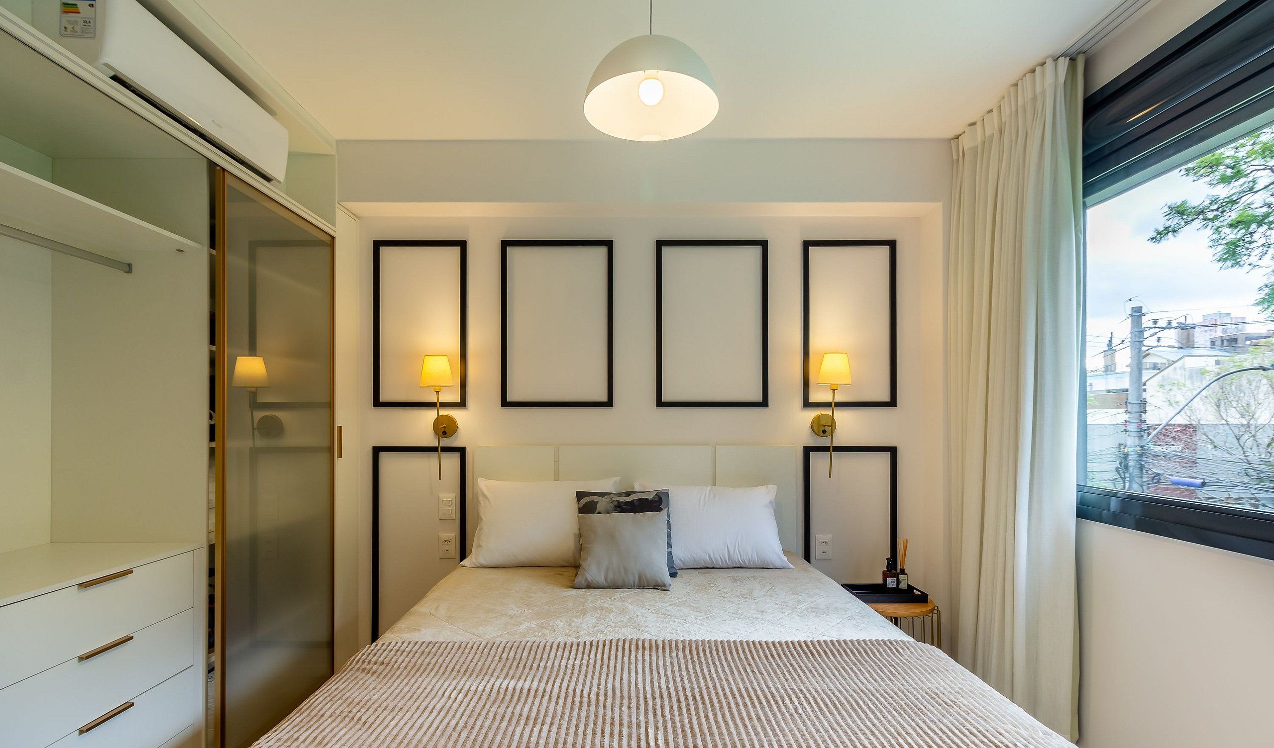 Quarto de hotel com uma cama, abajures, uma janela com cortinas e vista para a paisagem urbana.