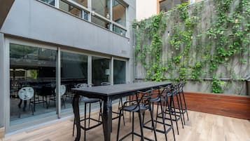 A modern outdoor dining area with a long table and chairs, a glass partition, and a wall covered in climbing plants.