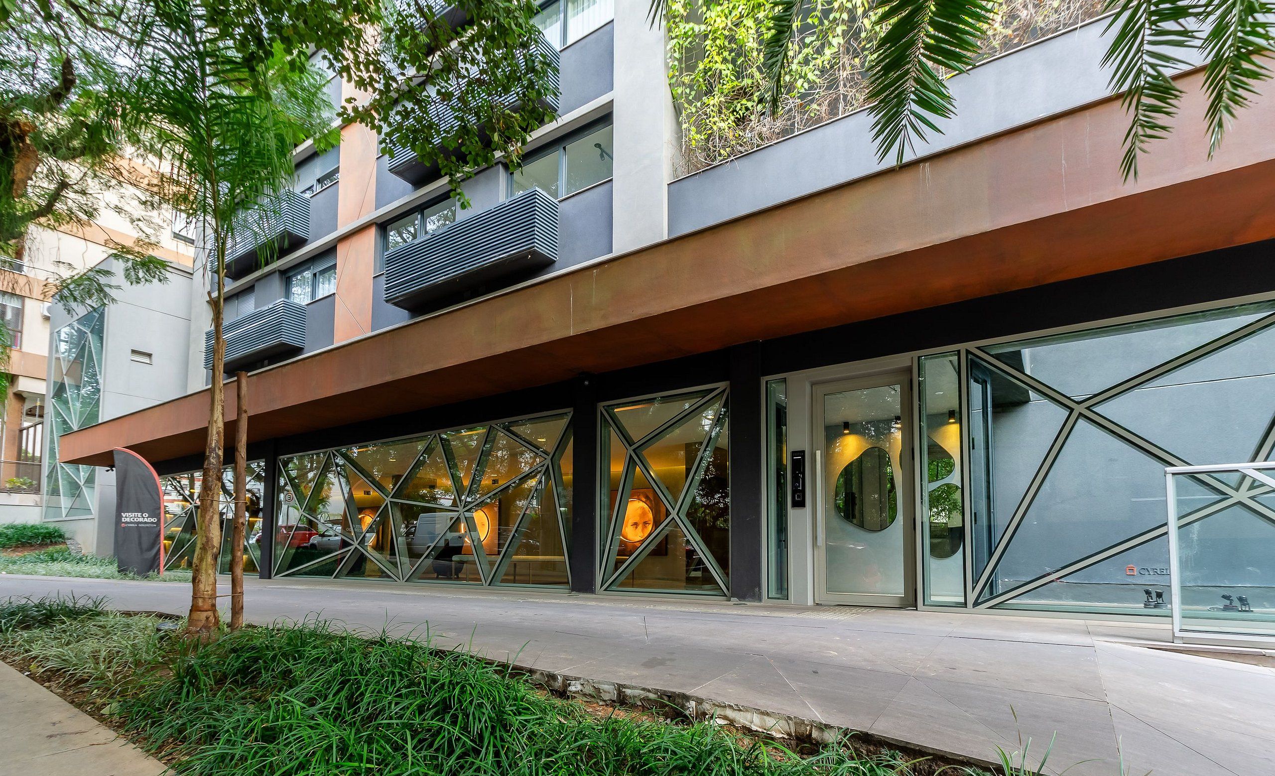 Un edificio moderno con fachada de vidrio, zona de estar al aire libre y una combinación de espacios verdes y elementos arquitectónicos.