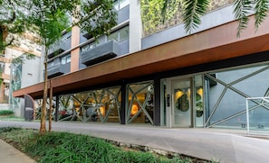 Un bâtiment moderne doté d’une façade en verre, d’un espace extérieur aménagé pour s’asseoir et d’un mélange d’éléments végétaux et architecturaux.