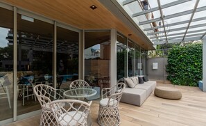 Une terrasse extérieure moderne, dotée de meubles en osier, d’une table en verre et d’un canapé.