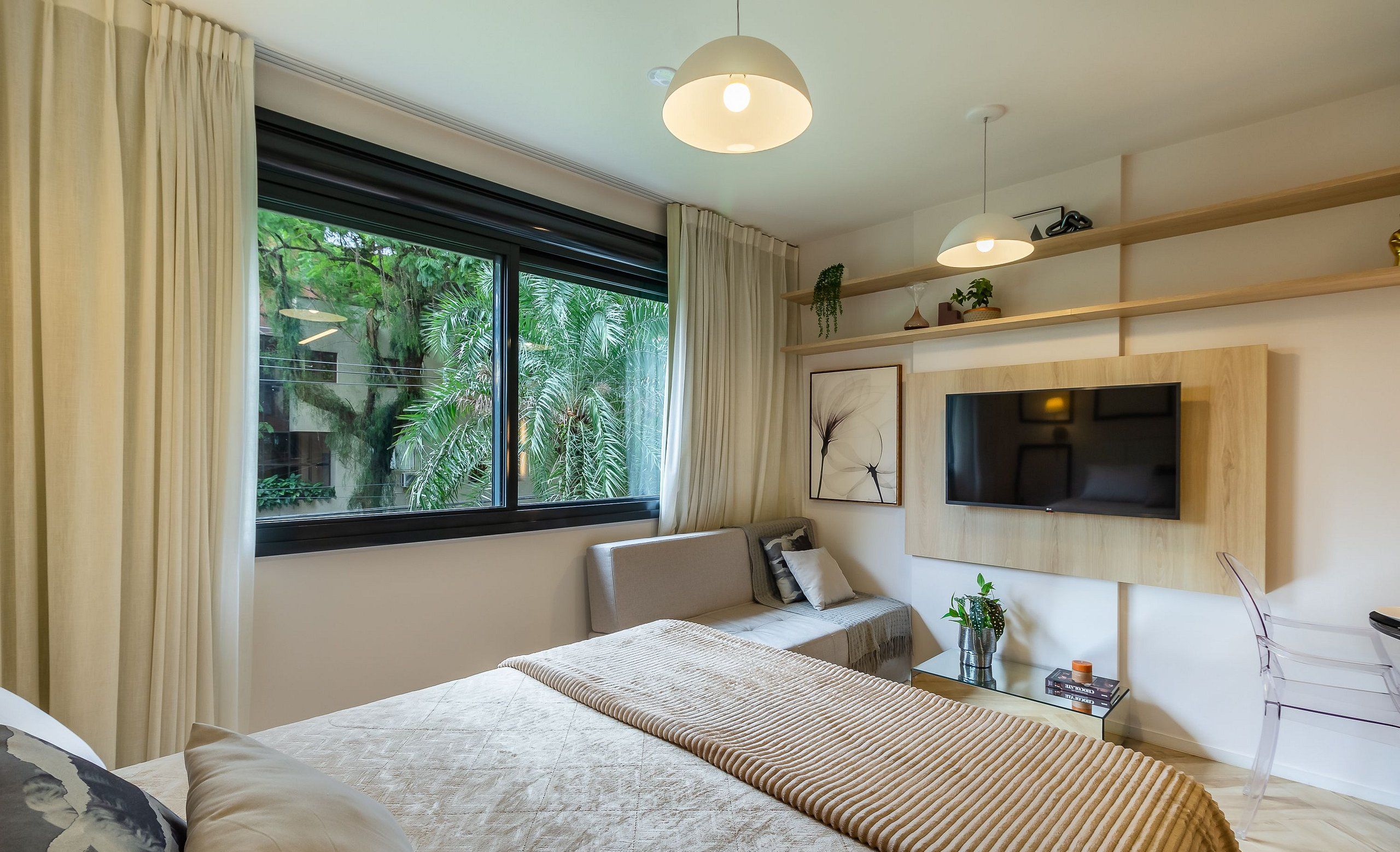 A modern bedroom with a large bed, a TV mounted on the wall, and a window with curtains.