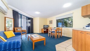 A compact living area with a sofa, a dining table with chairs, a TV, and a kitchenette.