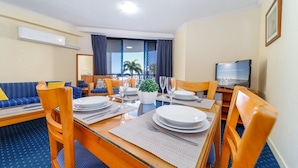 A hotel room with a dining area, a sofa, a TV, and a window with curtains.