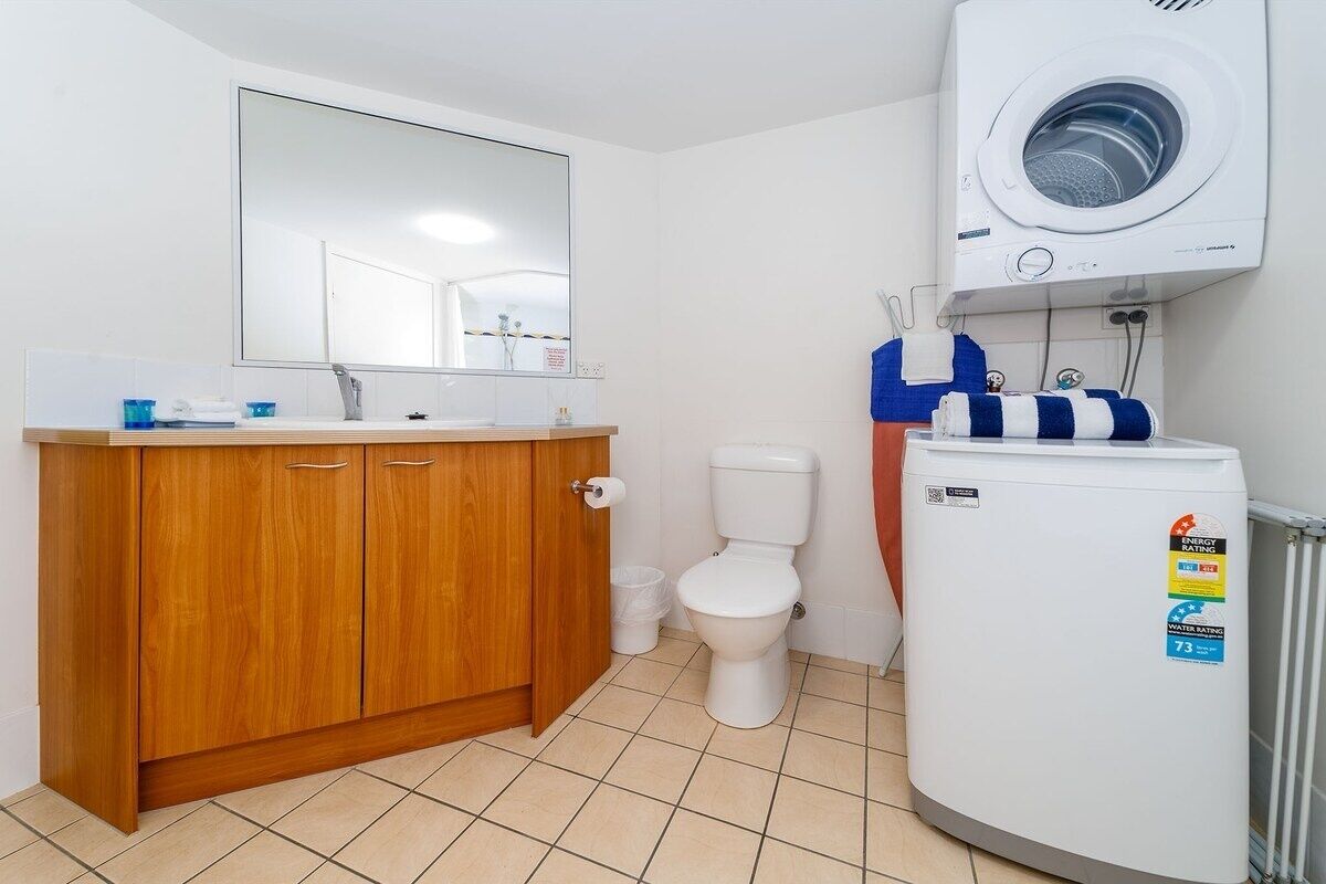 Une salle de bain avec un meuble-lavabo en bois, des toilettes, un lave-linge et un radiateur.