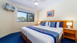 A hotel room with a large bed, a ceiling fan, a TV mounted on the wall, and a window with a view of greenery.
