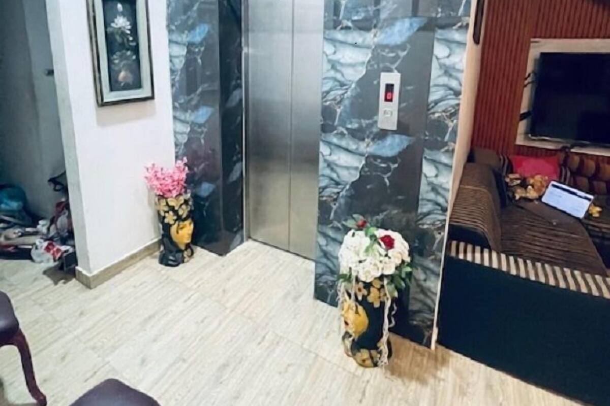 Un vestíbulo de hotel con pared de mármol, un ascensor, un cuadro enmarcado y un sofá con televisor.