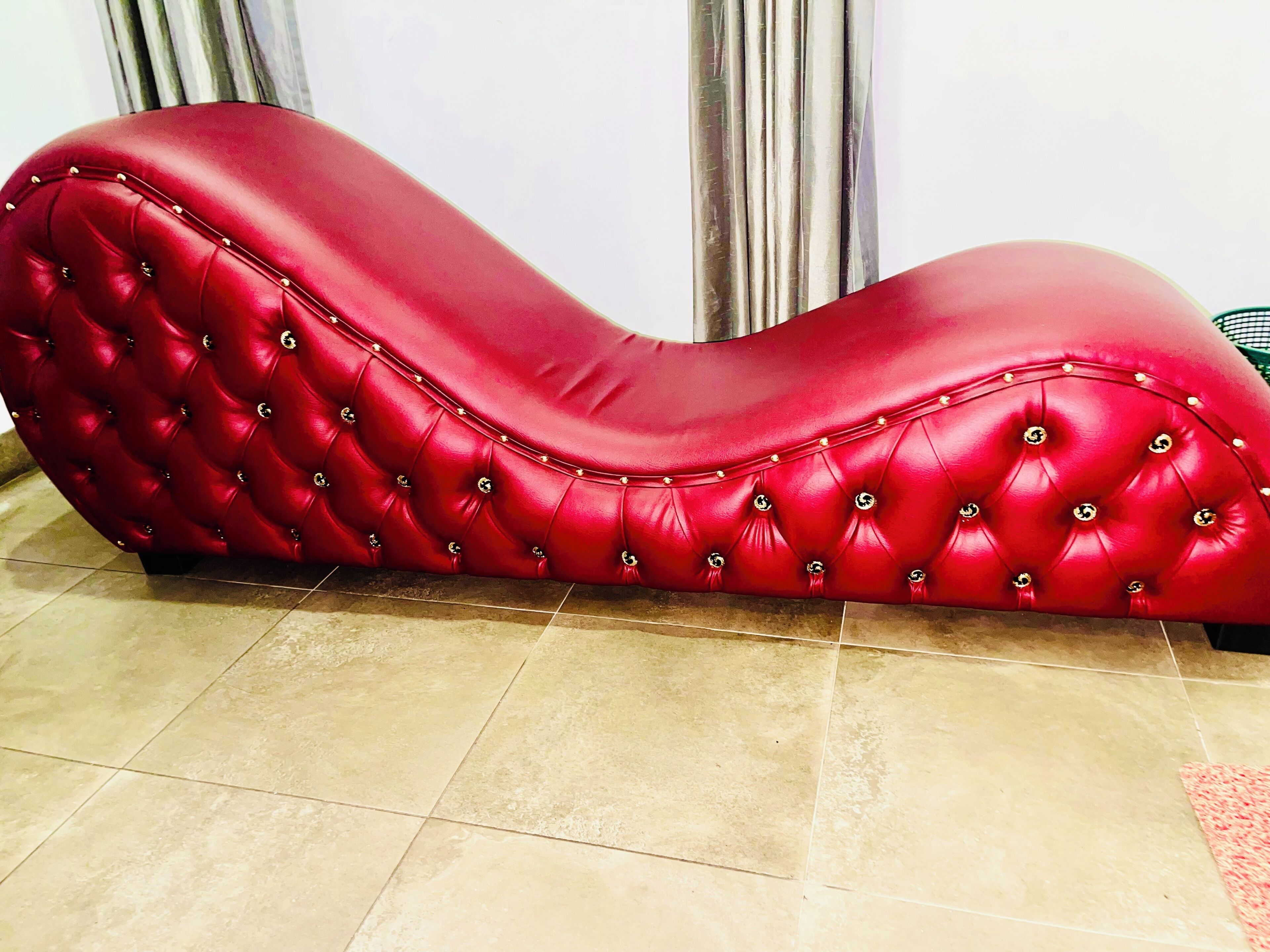 Un sofá rojo con capitoné y diseño curvo, sobre un piso de baldosas.