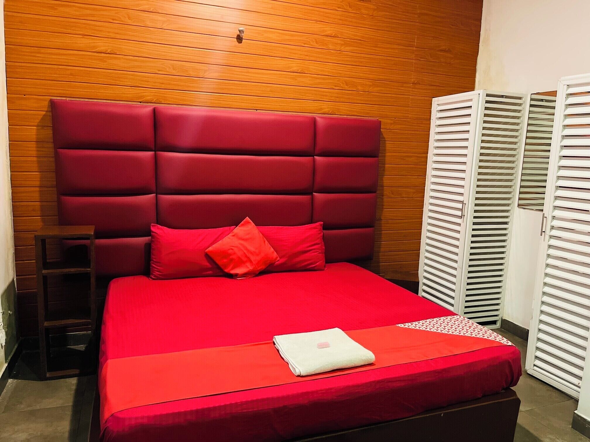 A room with a red upholstered headboard, a red bedspread, and a white towel on the bed.