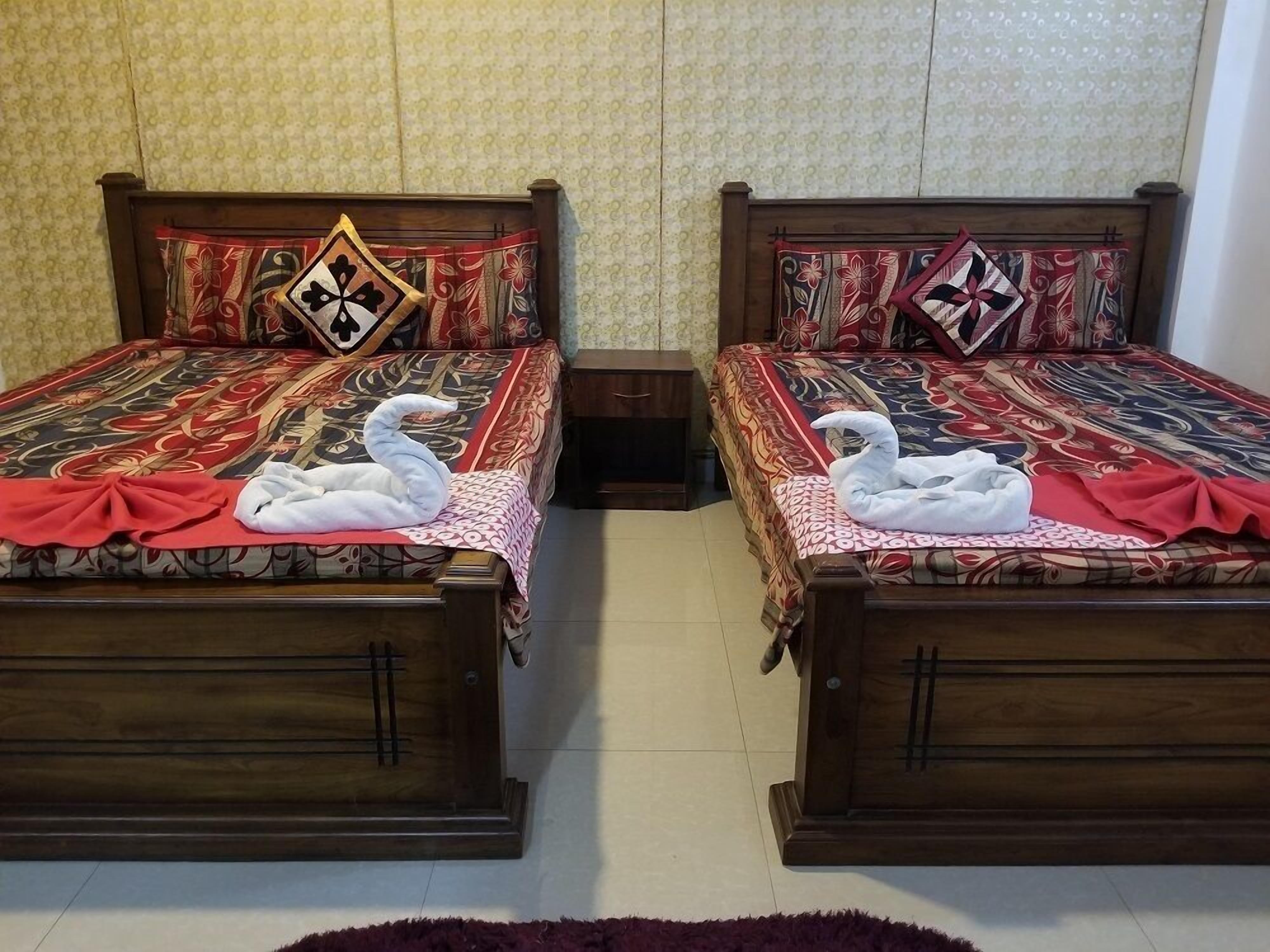 Dos camas iguales con ropa de cama estampada con motivos florales y almohadas decorativas; cada cama tiene una toalla con forma de cisne.