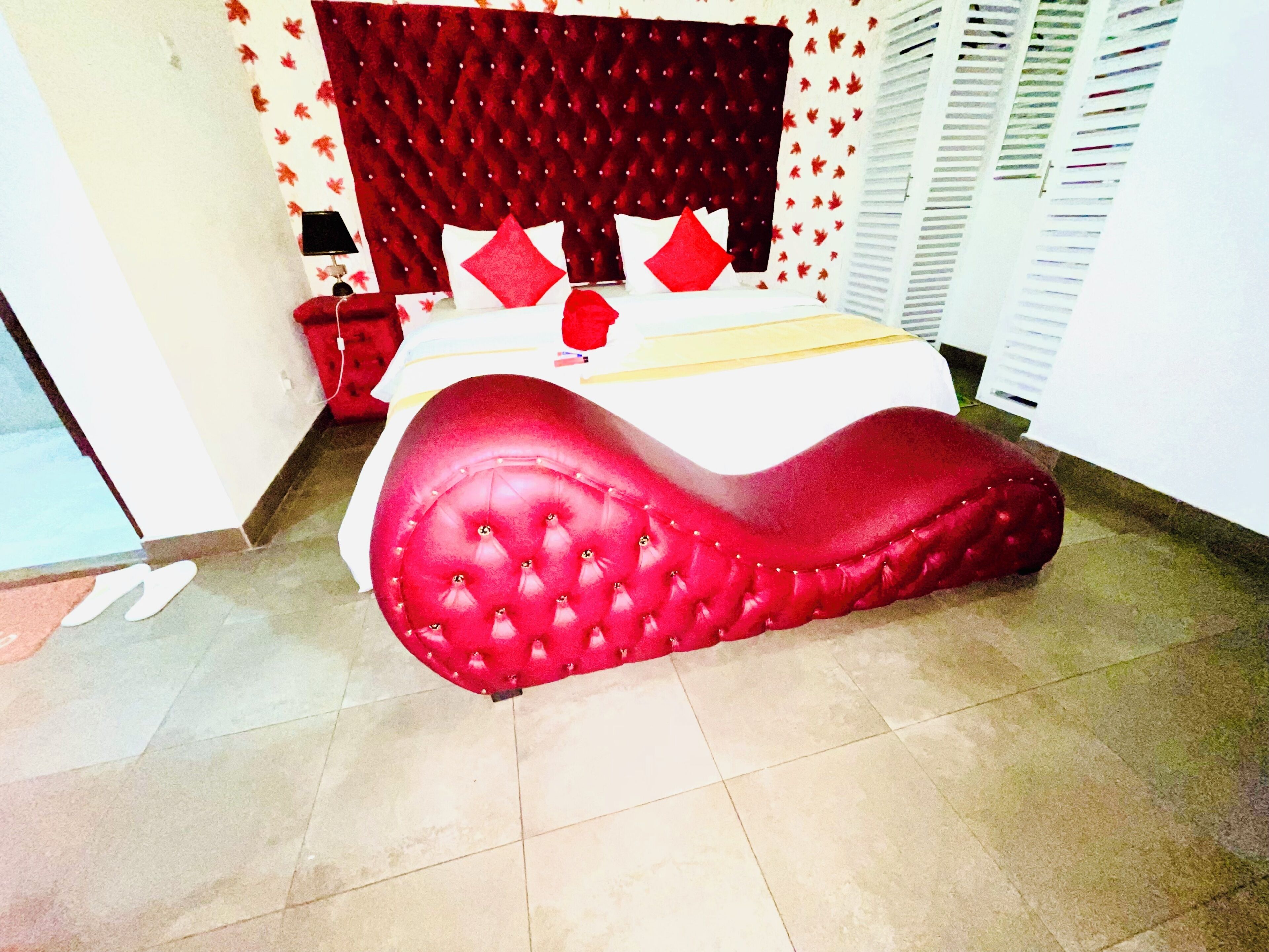 A bed with a red headboard and white bedding, a red upholstered bench, and a tiled floor.