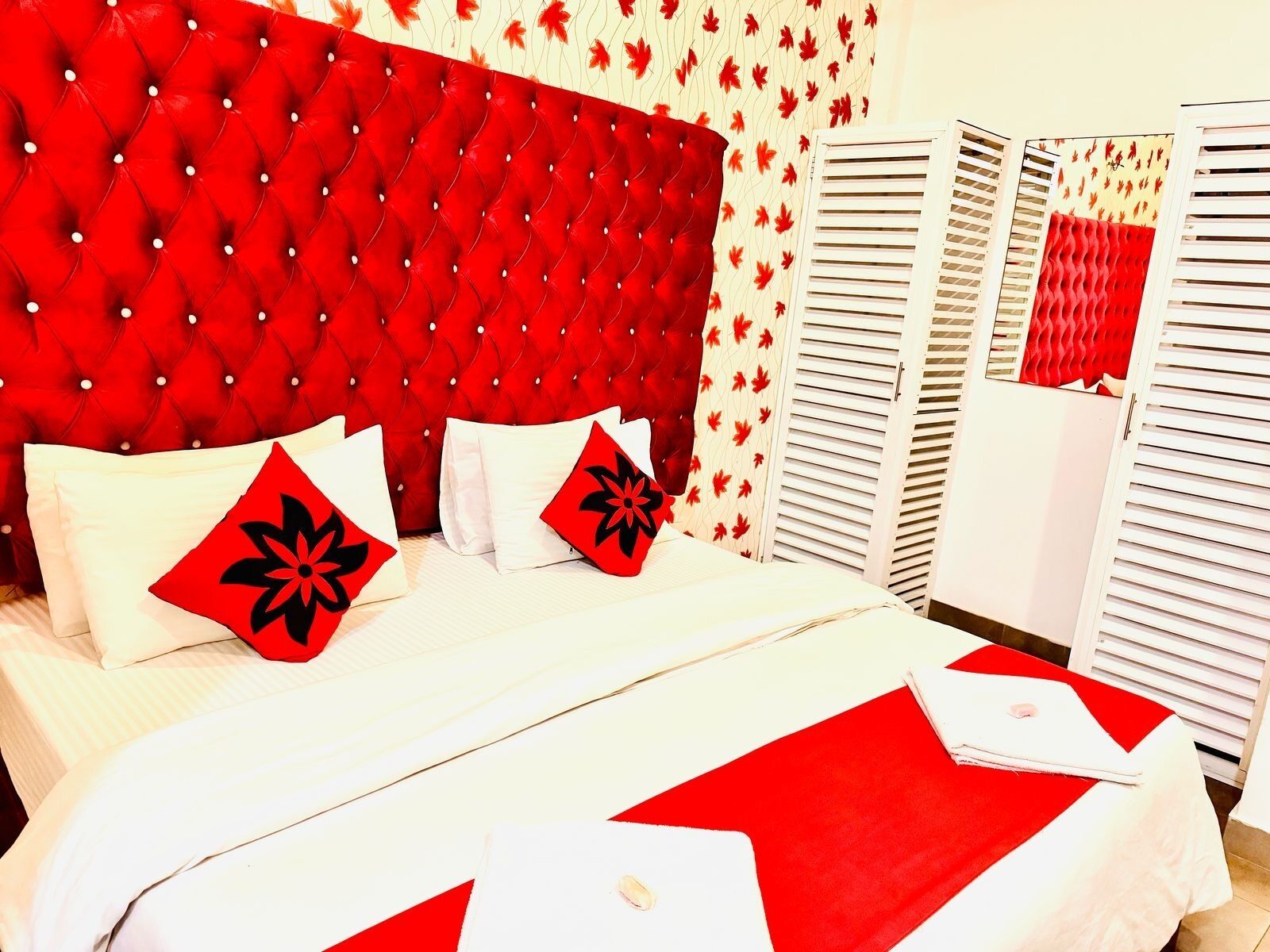 A hotel room with a tufted red headboard, white bedding, and red and white patterned curtains.