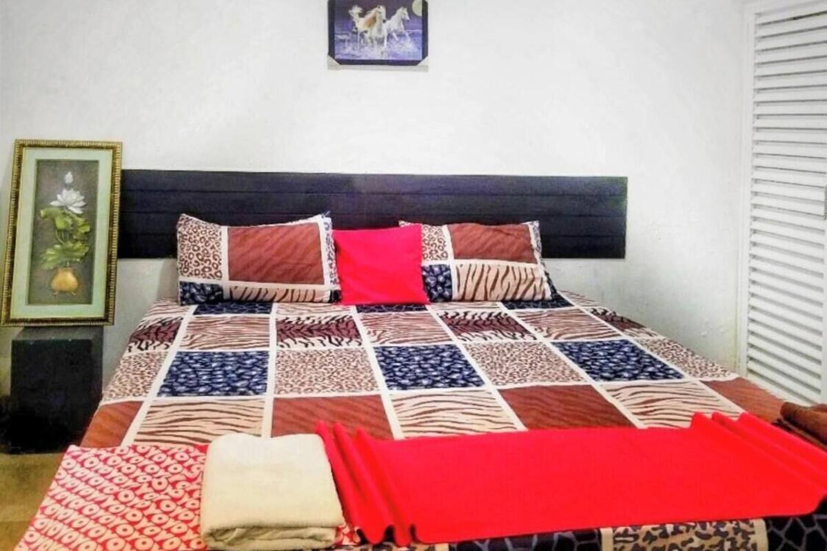 Un dormitorio con una cama grande, cabecero, un cuadro enmarcado en la pared y una ventana con persianas.