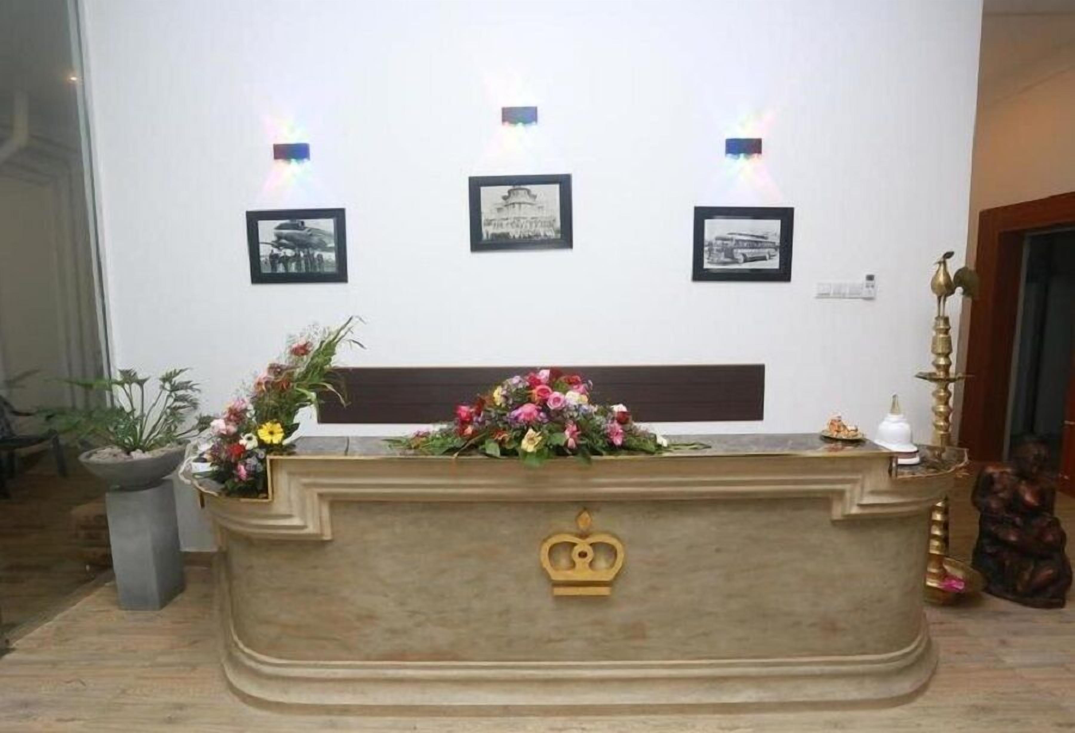 A reception desk with a crown emblem, three framed photographs on the wall, and a floral arrangement on the desk.