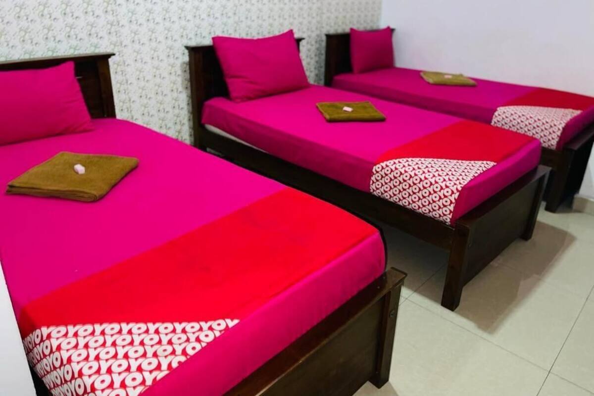 Tres camas individuales con ropa de cama rosa brillante y cabeceros de madera en una habitación con papel tapiz estampado.