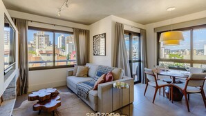 A modern living room with a sofa, dining table, and chairs. Large windows offer a city view. - Comfort and a Beautiful View! Pgr1101 (Porto Alegre)