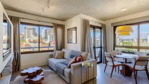 Ein modernes Wohnzimmer mit einer Couch, einem Esstisch und Stühlen. Große Fenster bieten Blick auf die Stadt.